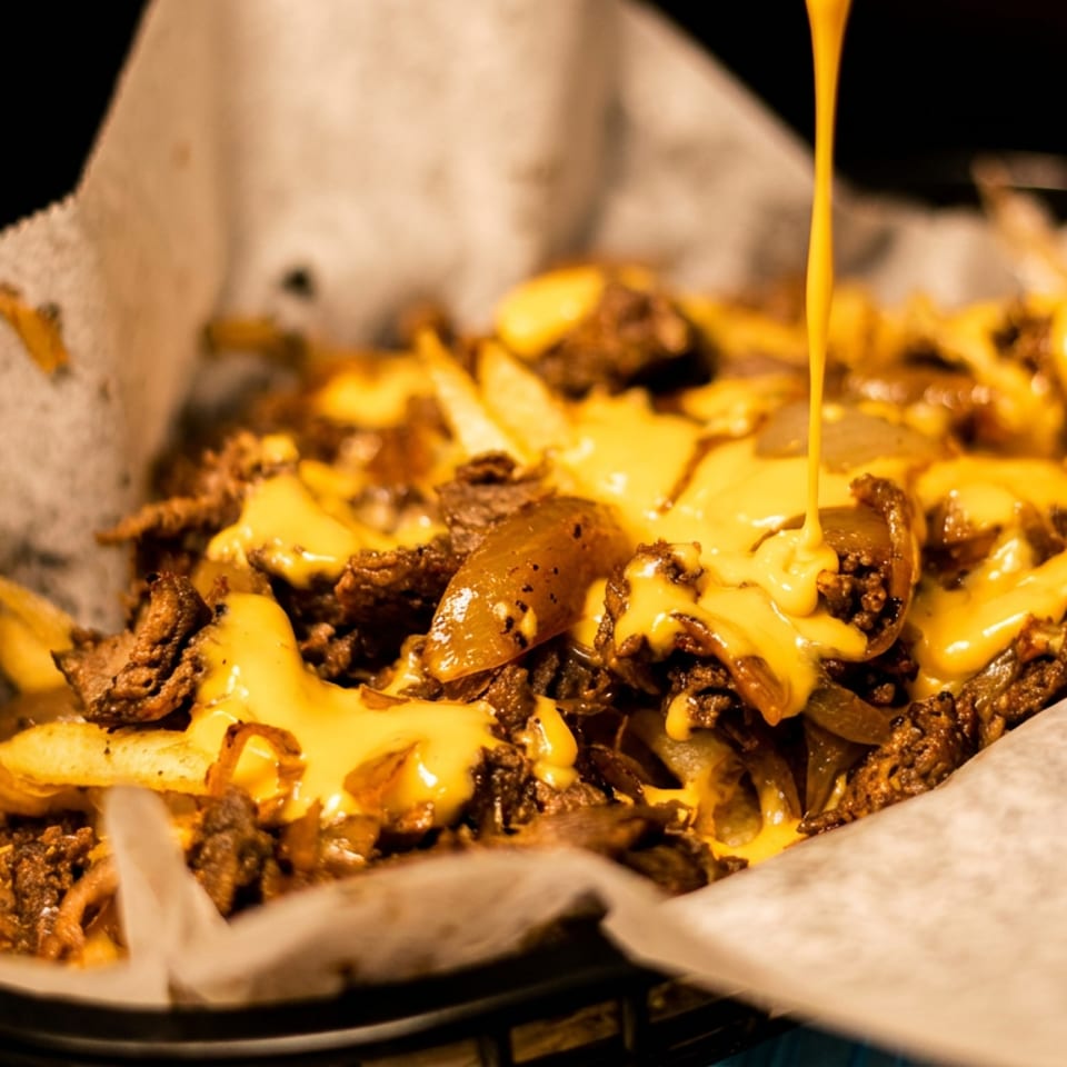 Loaded fries topped with seasoned meat, sautéed onions, melted cheese, and cheese sauce in a paper-lined basket.