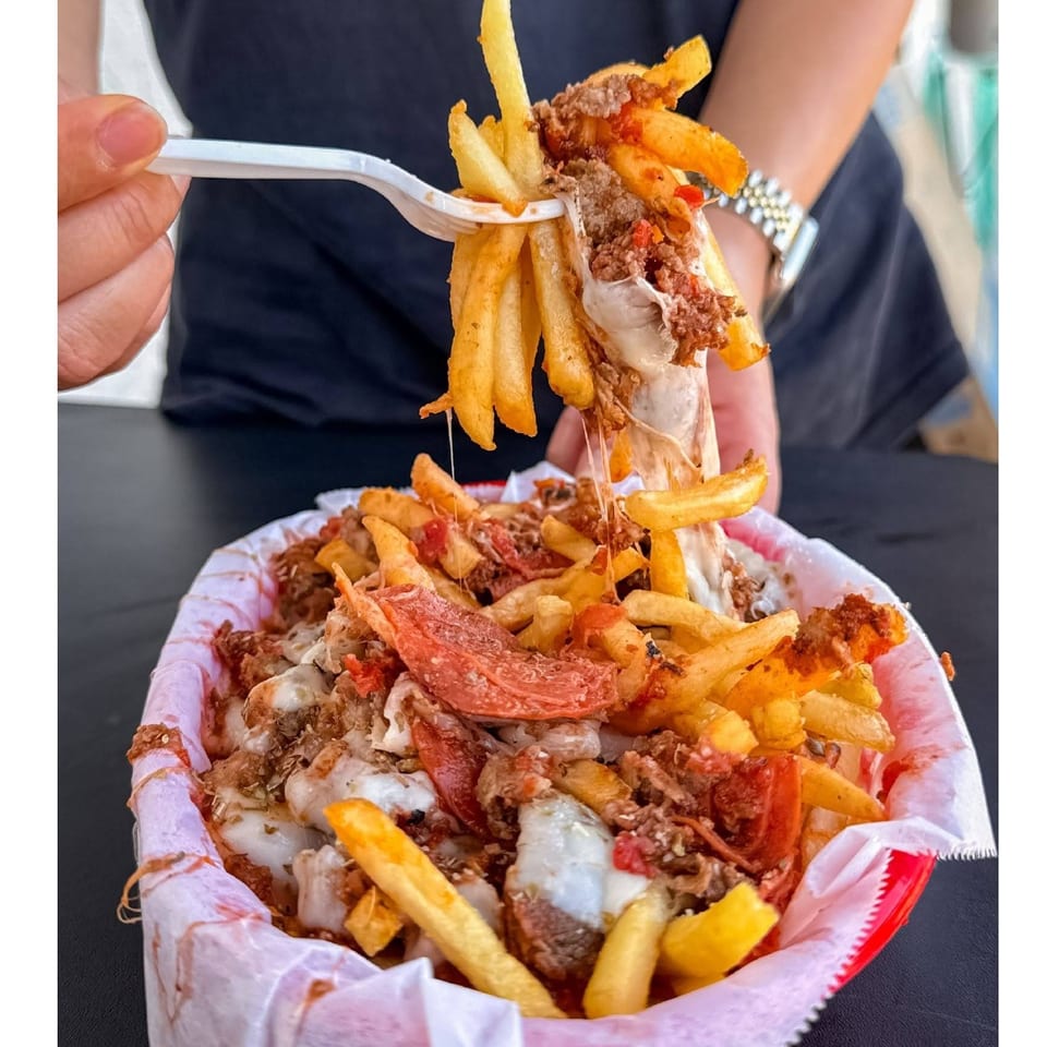 Loaded fries topped with meat, melted cheese, tomatoes, and sauce, with a fork lifting a bite above the serving bowl.